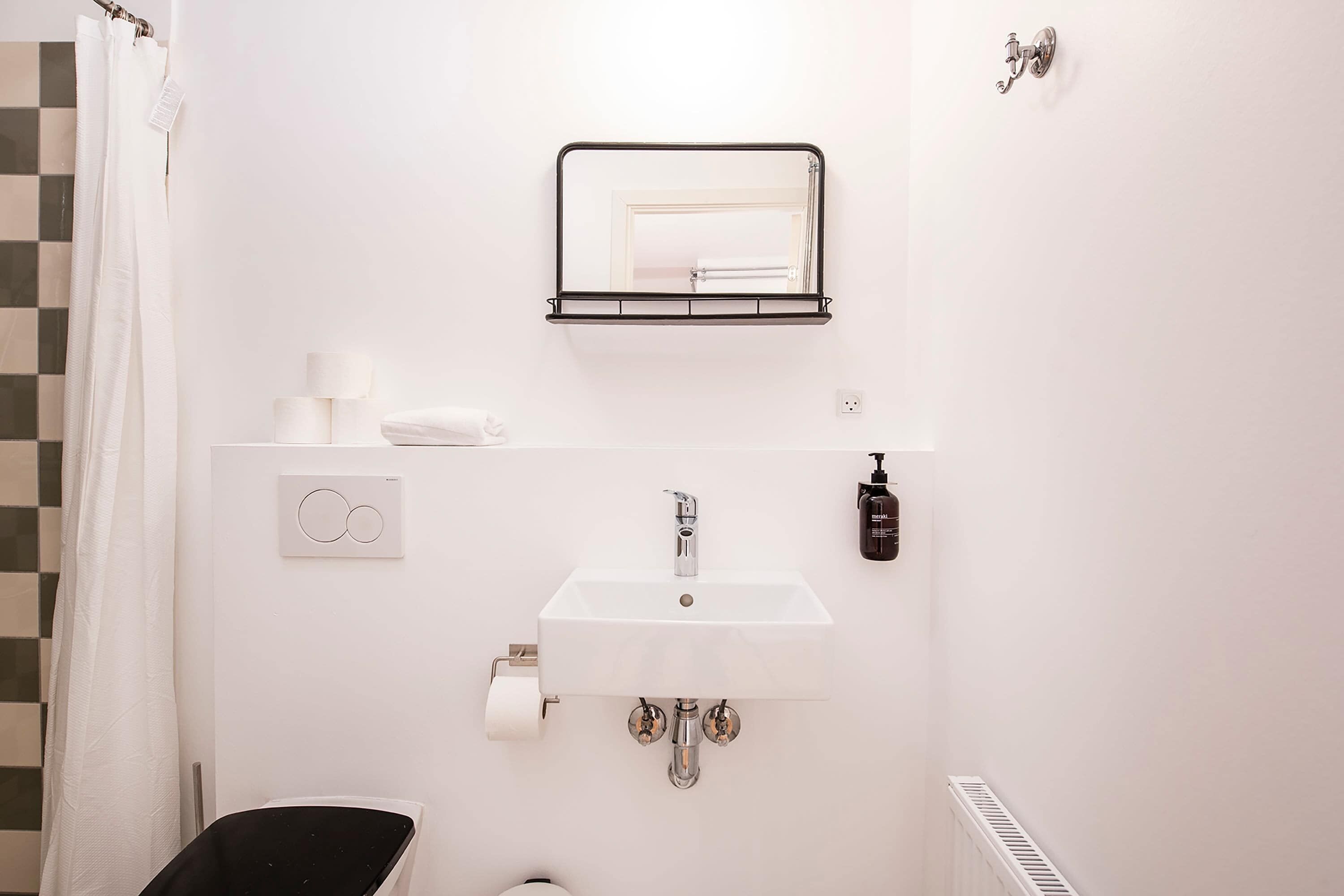 A bathroom with a white sink, a mirror, a towel rack, a toilet, and a shower curtain.