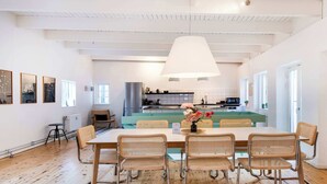 Een ruime eethoek met een houten tafel, rieten stoelen, een grote hanglamp en uitzicht op de keuken.