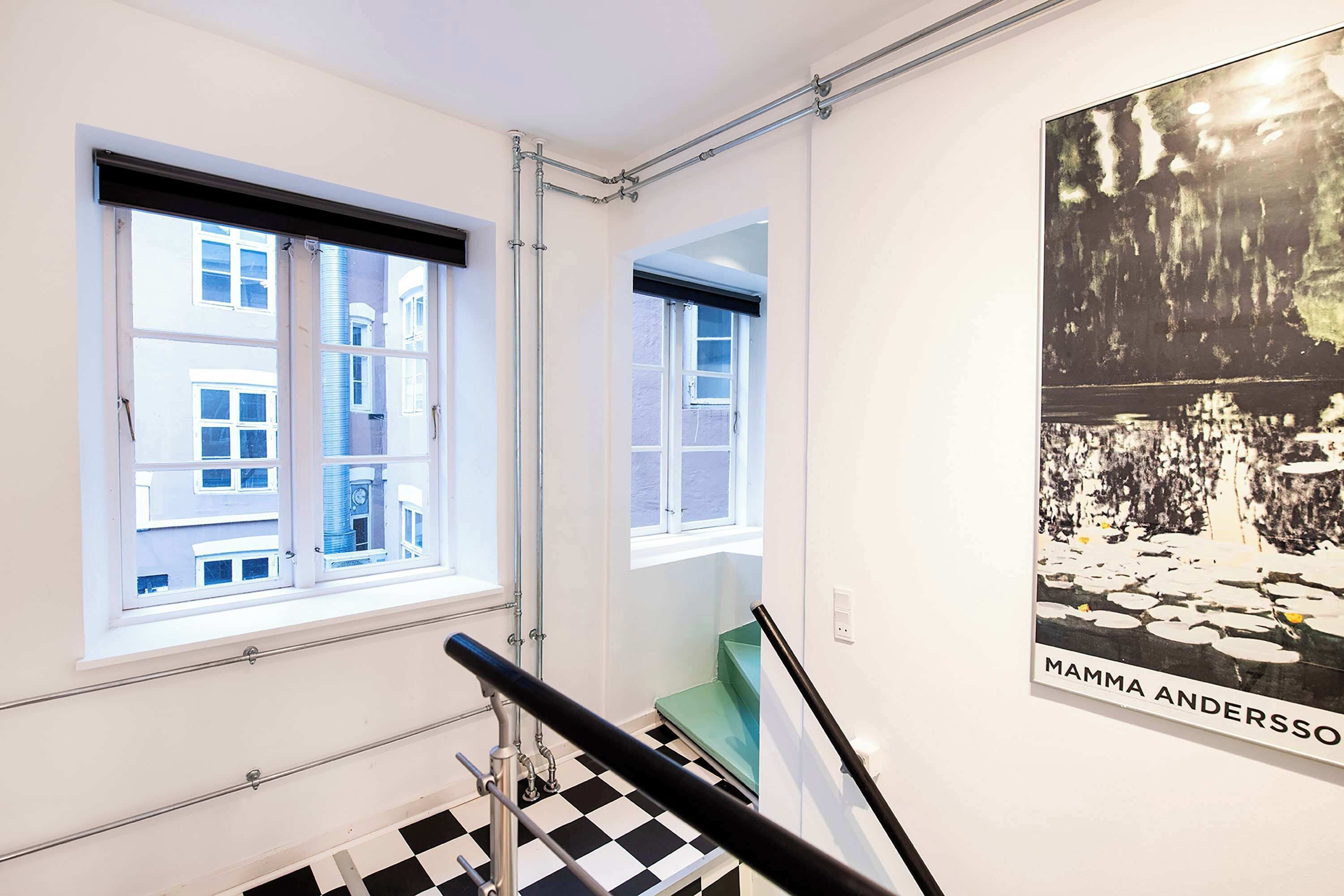 Ein Zimmer mit Schachbrettmuster-Boden, einem Fenster mit Blick auf Gebäude und einem Poster an der Wand.