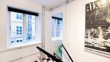 Ein Zimmer mit Schachbrettmuster-Boden, einem Fenster mit Blick auf Gebäude und einem Poster an der Wand.