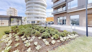 Een modern gebouw met een cirkelvormig ontwerp, een aangelegde tuin met diverse planten en een parkeerplaats met fietsen.