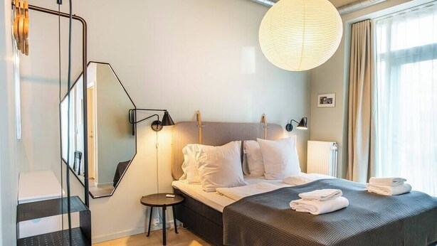Hotelkamer met een bed, nachtkastjes, een spiegel, een hanglamp en uitzicht op het buiten.