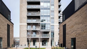 Een meerlaags woongebouw met balkons, een bakstenen gevel en een centrale binnentuin met bomen en een pad.