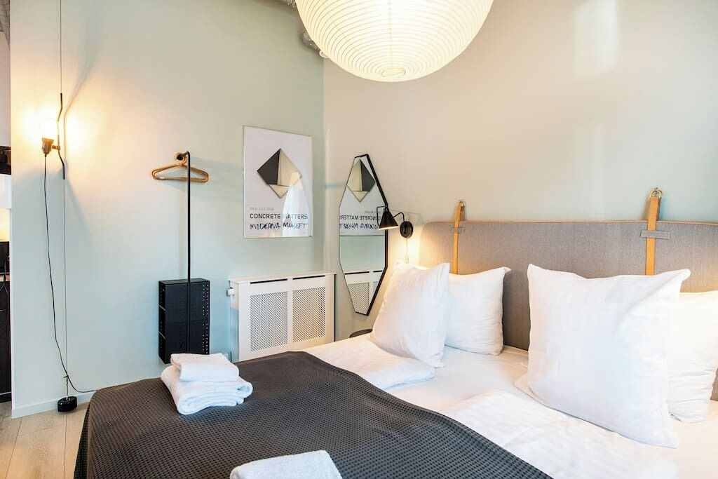 Ett modernt hotellrum med en stor säng, ett sängbord, en lampa och en väggmonterad värmare.
