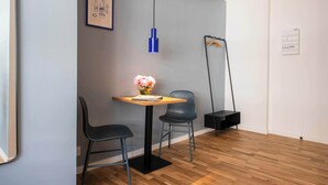 A modern room with a wooden floor, a round table with two chairs, a blue pendant light, and a framed picture on the wall.