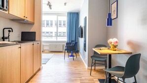 A modern kitchen with wooden cabinets, a black countertop, and a built-in microwave. There is a dining area with a wooden table and chairs, and a window with blue curtains. - The Lakes Studio by Daniel & Jacob's (København)