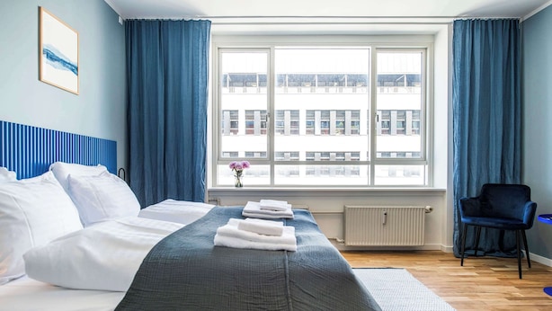A hotel room with a large bed, a window with curtains, a radiator, and a chair. - The Lakes Studio by Daniel & Jacob's (København)