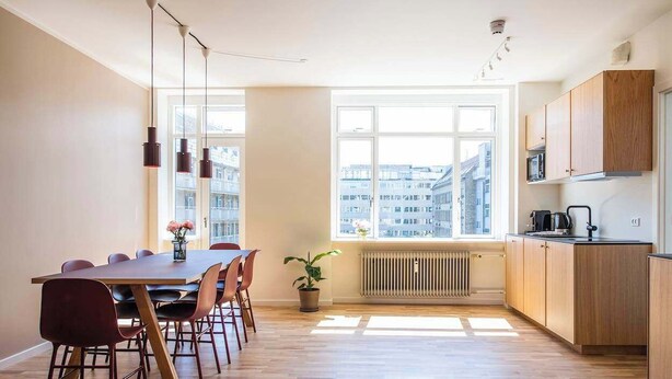 Une cuisine moderne avec des meubles en bois, une table à manger avec des chaises et une grande fenêtre donnant sur la ville.