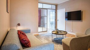 Un salon moderne avec un canapé gris, un coussin rouge, une table basse et un téléviseur à écran plat fixé au mur.