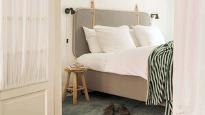 A bed with a headboard, a bedside table with books and glasses, and a pair of shoes on the floor.