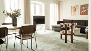 A living room with a sofa, a coffee table, a TV, a dining table with chairs, and a vase with flowers.