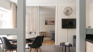 A modern living room with a dining area, a flat-screen TV mounted on the wall, and a standing fan. - The Brewer apartments by Daniel&Jacob's (København)
