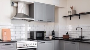 A kitchen with grey cabinets, a stainless steel range hood, a microwave, a coffee maker, and a sink. - The Brewer apartments by Daniel&Jacob's (København)