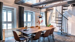 Ein stilvoller Essbereich mit Holztisch und -stühlen, einer Vase mit Blumen und einer Treppe mit Metallgeländer.