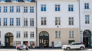 Eine Reihe weißer Gebäude mit zahlreichen Fenstern und Türen, ein geparktes Auto und ein buntes Fahrzeug davor.