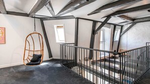 Ein modernes Interieur mit freiliegenden Balken, einem Hängekorbsessel und einer Treppe.