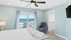 A bedroom with a bed, a chair, a ceiling fan, and a view of the ocean through a sliding door.