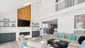 A spacious living room with a high ceiling, a TV mounted on the wall, and a balcony with a railing.