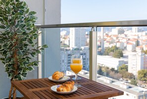 Een balkon met een houten tafel, een glas sinaasappelsap en twee croissants op borden.