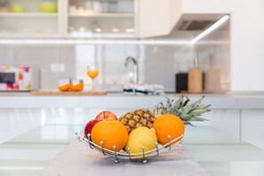 Uma tigela de frutas sobre uma mesa, com uma cozinha ao fundo.