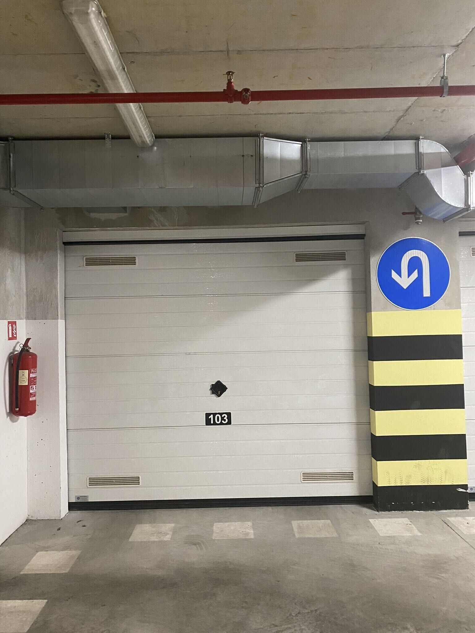 A fire exit door with a number 103 sign, a fire extinguisher, and a directional sign with a curved arrow.