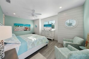 Un dormitorio con cama, cómoda, silla y un cuadro de una playa.