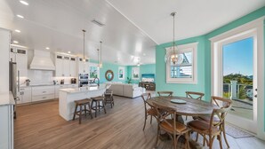 A modern kitchen with white cabinets, wooden flooring, and a central island with stools. - Bluetique:  Monthly luxury beach home, private pool, rooftop deck (Holmes Beach)