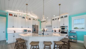 A modern kitchen with white cabinetry, a large island with stools, stainless steel appliances, and pendant lighting. - Bluetique:  Monthly luxury beach home, private pool, rooftop deck (Holmes Beach)
