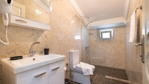 Een badkamer met een wit wastafelmeubel, spiegel en toilet, marmeren wanden en een douchegedeelte.