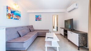 Een moderne woonkamer met een grijze bank, een witte salontafel, een televisie en een kast.