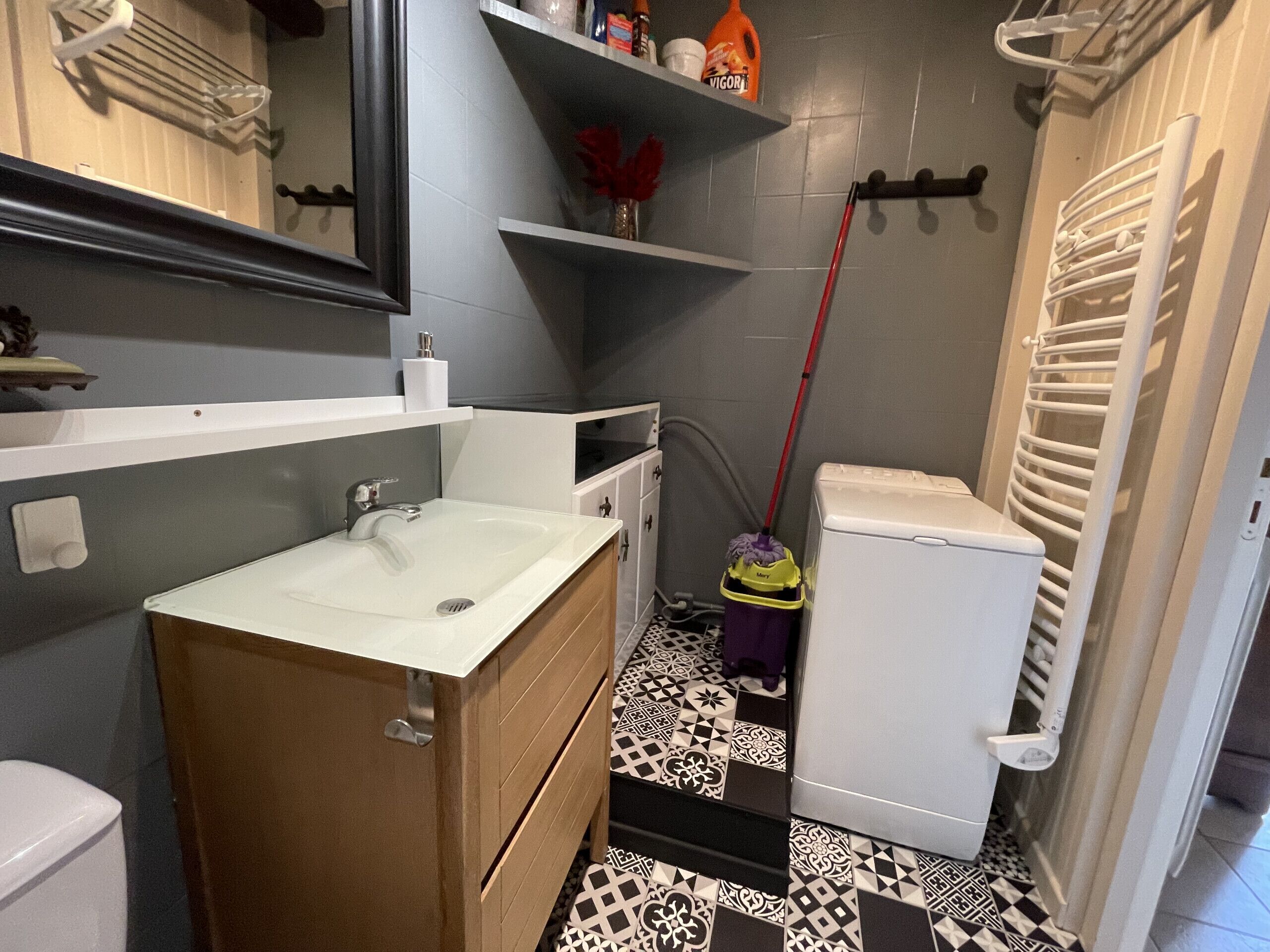 Une petite salle de bain avec un lavabo blanc, un meuble-lavabo en bois, des toilettes et un balai.