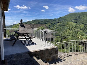 En balkon med et stentabel og bænke, der ud til et bjerglandskab.