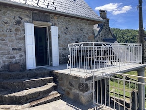 A stone building with a metal balcony and steps leading to a door.
