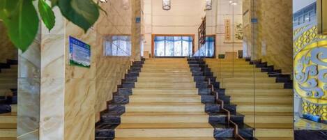 A grand staircase with marble and wooden steps leading to a bright interior space.