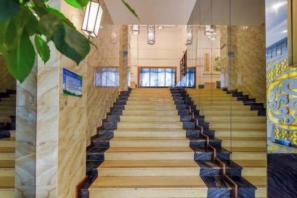 A grand staircase with marble and wooden steps leading to a bright interior space.