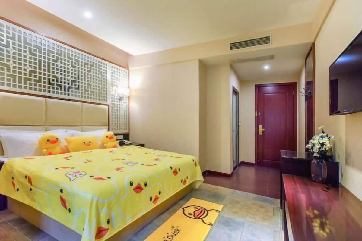 A hotel room with a bed, a TV, a wooden floor, a decorative wall panel, and a door.