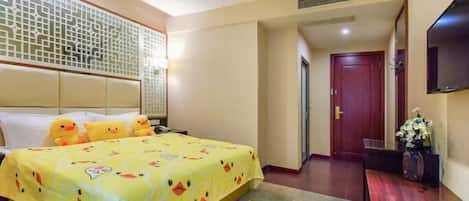 A hotel room with a bed, a TV, a wooden floor, a decorative wall panel, and a door.