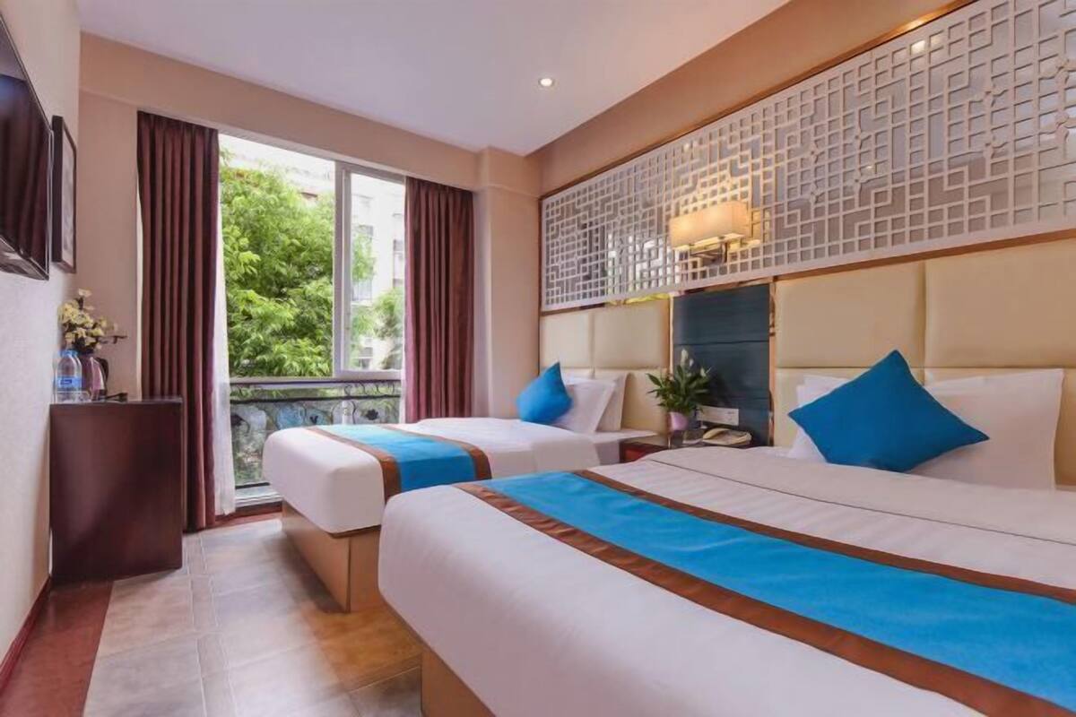 A hotel room with two beds, a balcony, a decorative wall, and a view of greenery.