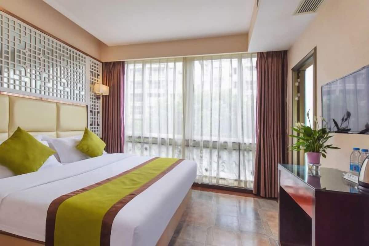 A hotel room with a large bed, a desk with a computer, a TV, and a balcony with curtains.