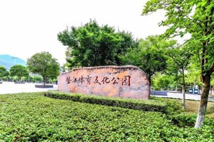 Placa de pedra com caracteres chineses, cercada por sebes e árvores bem cuidadas.