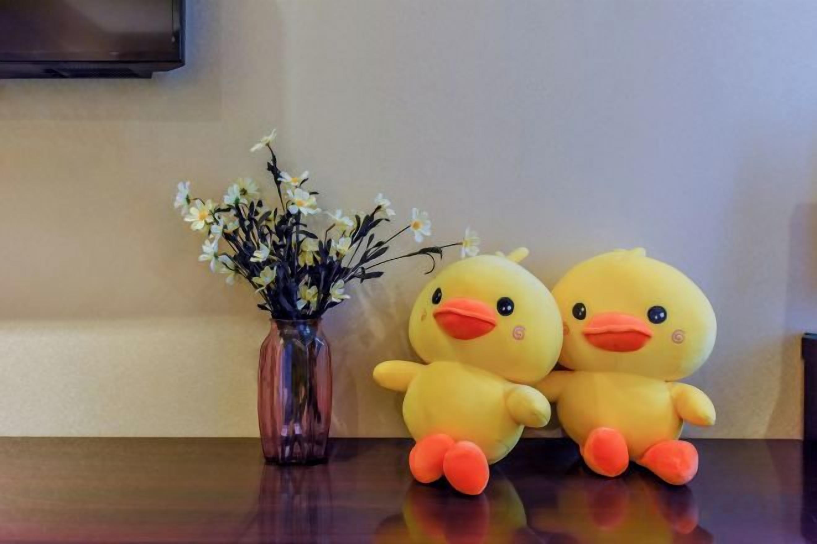A table with a vase of flowers and two plush duck toys.