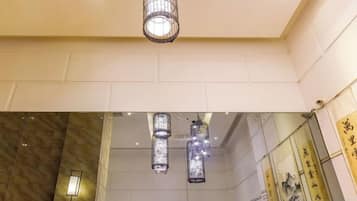 A hotel lobby with a high ceiling, a hanging light fixture, and a wall with calligraphy.