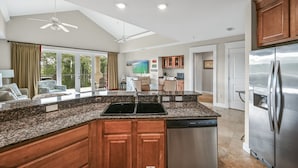 A spacious kitchen with granite countertops, wooden cabinets, a stainless steel refrigerator, and a ceiling fan. - Golf Cart ~ Golf Course View ~ Community Pool (Miramar Beach)