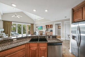 A spacious kitchen with granite countertops, wooden cabinets, a stainless steel refrigerator, and a ceiling fan.