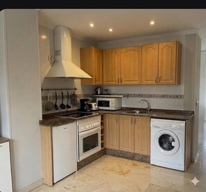 A compact kitchen with a stove, microwave, sink, and washing machine.