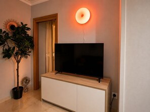 A television on a wooden cabinet, a potted plant, and a wall-mounted light fixture.