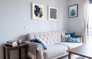 A living room with a sofa, a coffee table, a side table with books and a candle, and two framed artworks on the wall.