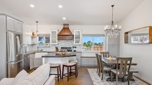 Una cocina moderna con una isla central, muebles blancos, electrodomésticos de acero inoxidable y una lámpara de araña.