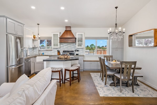 A modern kitchen with a central island, white cabinetry, stainless steel appliances, and a chandelier.