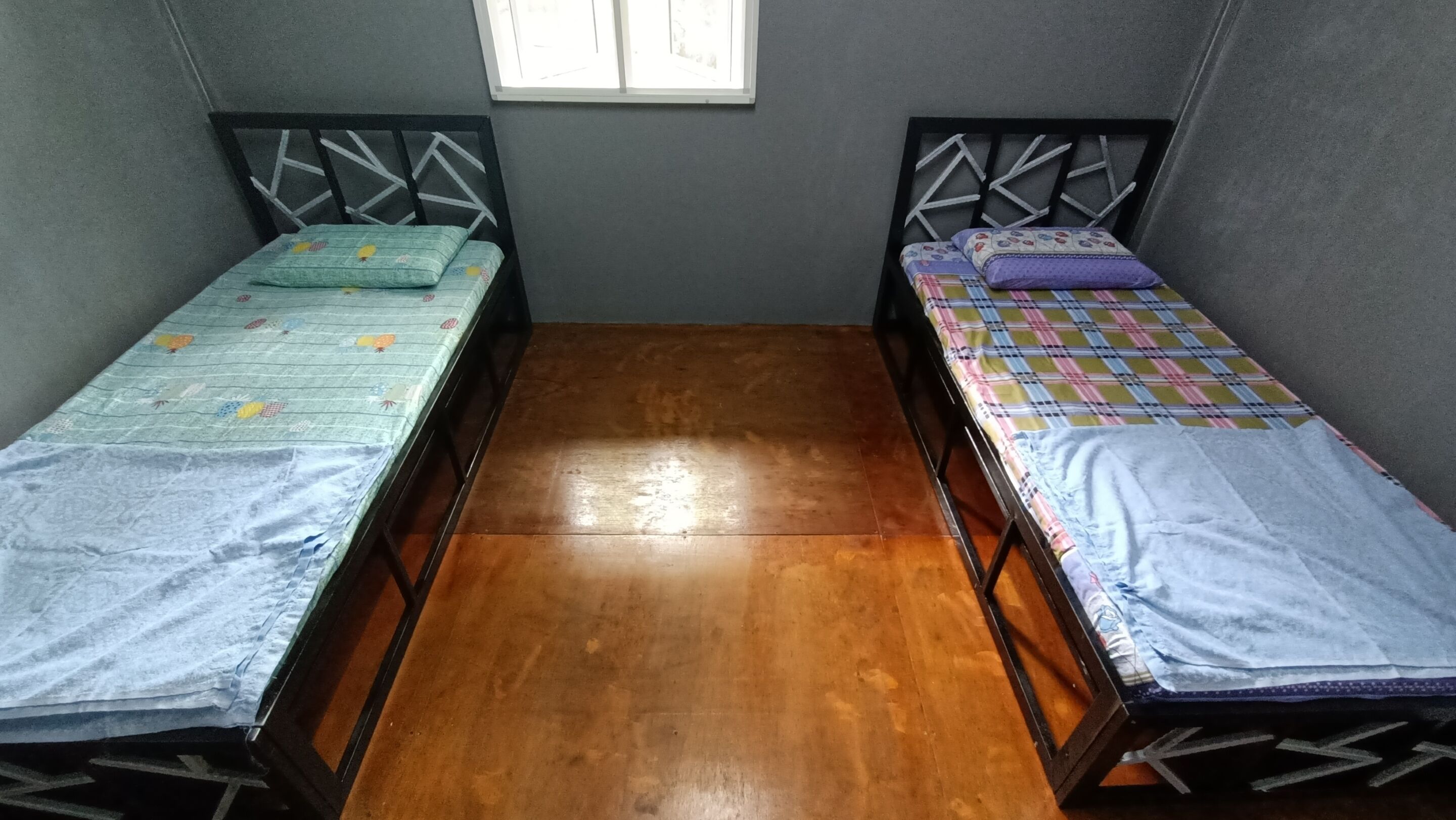 Pequeña habitación con dos camas individuales, suelo de madera y una ventana.